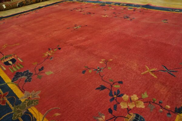 Red rug with low pile and scattered floral vines, featuring a navy and yellow border on a wood floor.