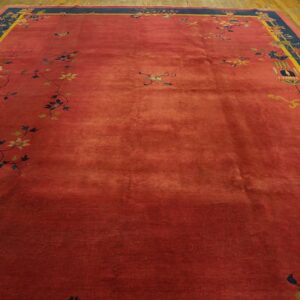 Rust-colored rug featuring scattered floral vines and a wide navy and yellow border on wood planks.