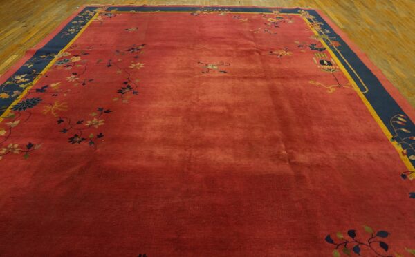 Rust-colored rug featuring scattered floral vines and a wide navy and yellow border on wood planks.