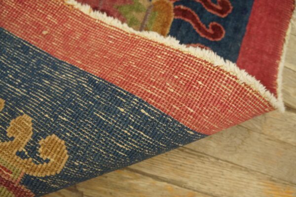 A rug is rolled back revealing its tightly woven red and blue foundation threads on rustic wood.