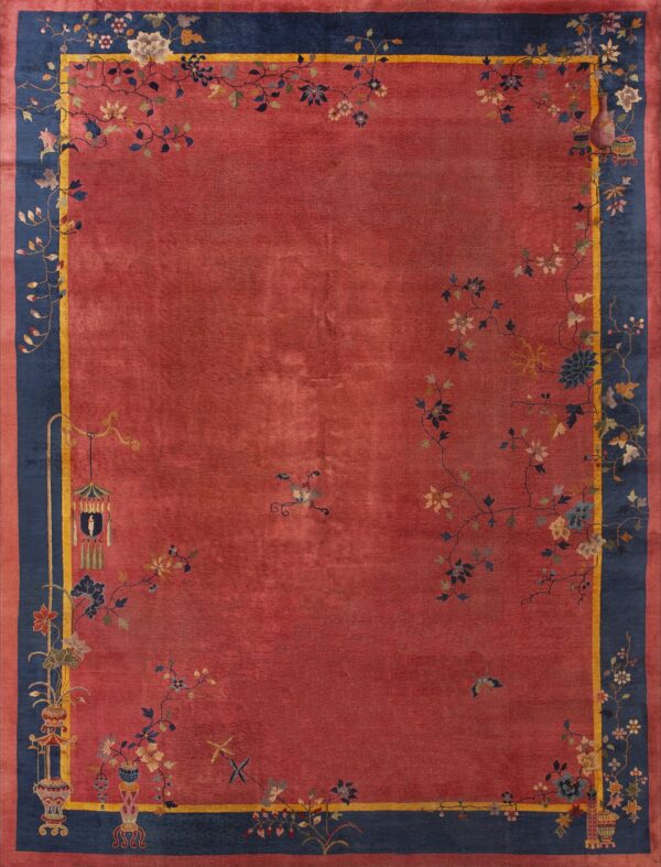 Reddish-pink rug with a wide navy border and yellow stripe accented by cascading floral and vase motifs.