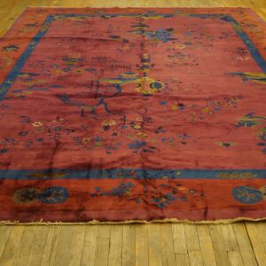 Maroon rug featuring detailed blue and yellow botanical and symbolic designs on yellow wood floors.