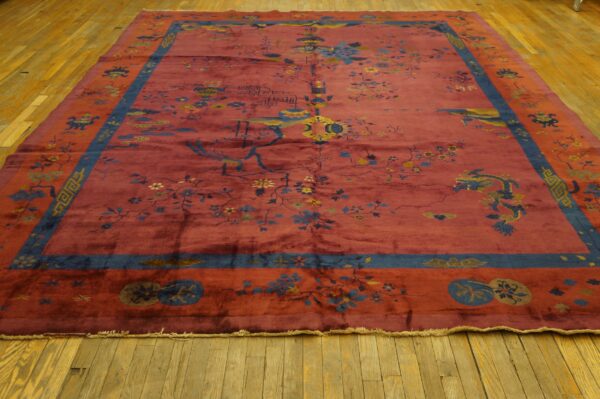 Maroon rug featuring detailed blue and yellow botanical and symbolic designs on yellow wood floors.