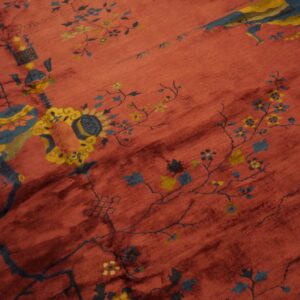 Reddish rug detail showing blue and yellow mythical creatures, flowering vines, and geometric elements.