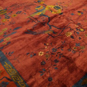 Rust colored rug displaying detailed blue and yellow floral motifs, a bird, and a wide blue patterned border.