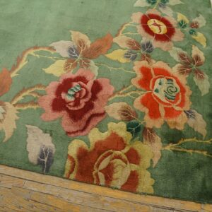 Floral rug in shades of green, red, pink, and yellow sits on distressed wood plank flooring.