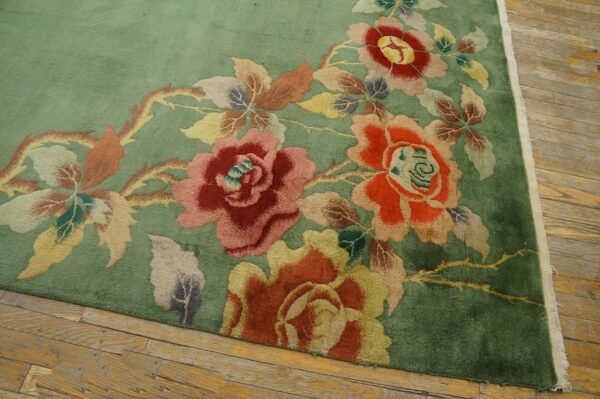 Floral rug in shades of green, red, pink, and yellow sits on distressed wood plank flooring.