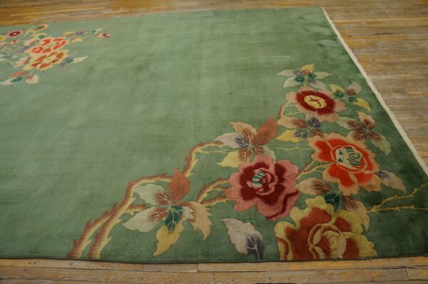 Plush sage green rug with large multicolored floral designs spreads across distressed wood flooring.