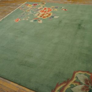 Sage green area rug with large colorful floral sprays in opposing corners on distressed wood plank flooring.