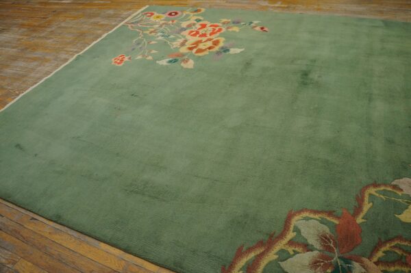 Sage green area rug with large colorful floral sprays in opposing corners on distressed wood plank flooring.