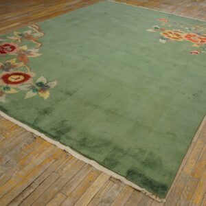 Green rug with large red and yellow floral border motifs displayed on distressed hardwood planks.