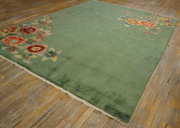 Green rug with large red and yellow floral border motifs displayed on distressed hardwood planks.