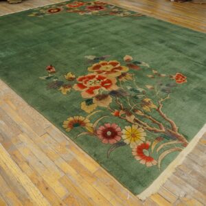 Sage green area rug with large red and gold floral sprays resting on light, distressed wood floors.