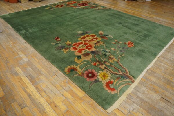 Sage green area rug with large red and gold floral sprays resting on light, distressed wood floors.