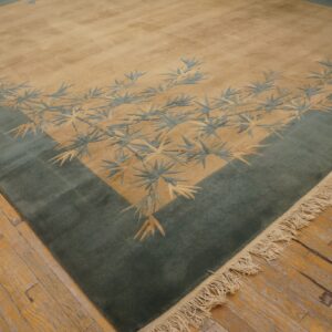 Tan field rug with a wide teal border and contrasting bamboo leaf motifs rests on distressed hardwood flooring.