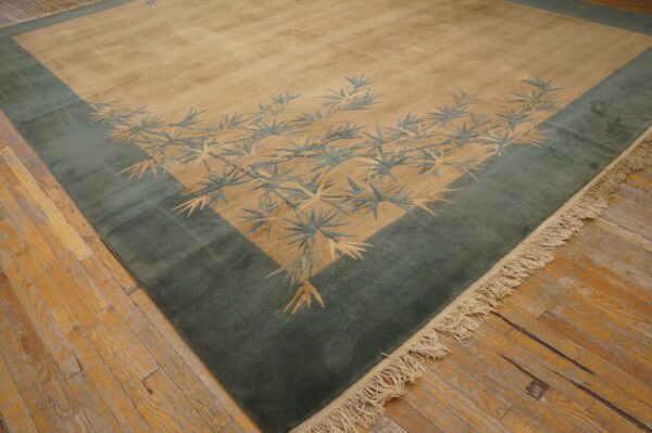 Tan field rug with a wide teal border and contrasting bamboo leaf motifs rests on distressed hardwood flooring.