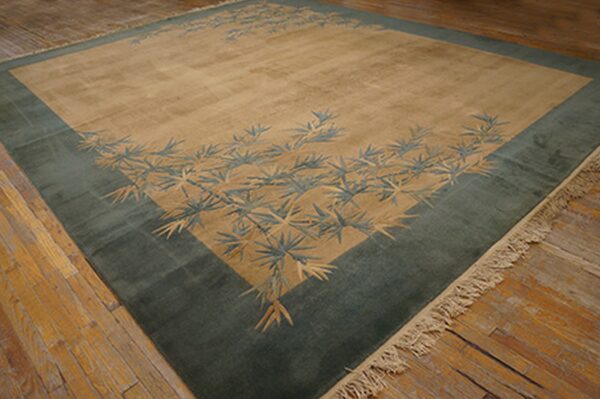 Beige rug with a wide teal-green border and stylized foliage pattern sits on distressed wood floors.