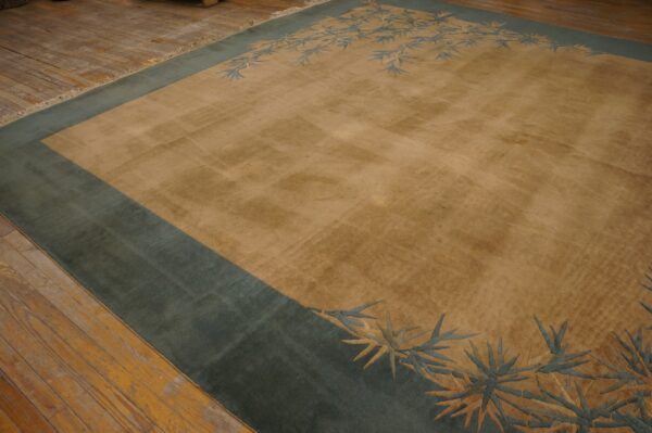 Tan area rug featuring a thick teal border and stylized blue foliage rests on a rustic wood floor.