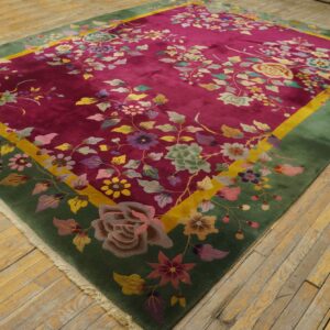 Deep pink floral rug with green and yellow borders displayed on distressed wood plank flooring.