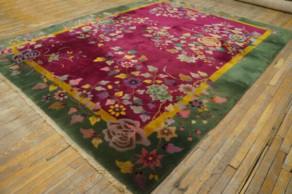 Deep pink floral rug with green and yellow borders displayed on distressed wood plank flooring.