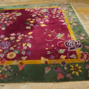 A deep magenta rug with a dense multicolored floral pattern and a wide green border lies on wood floors.