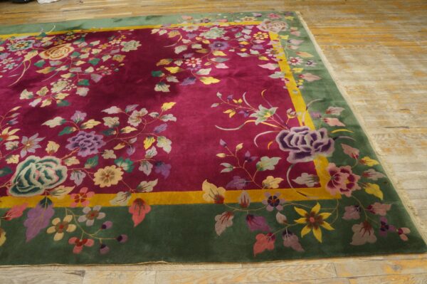 A deep magenta rug with a dense multicolored floral pattern and a wide green border lies on wood floors.