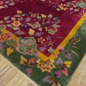 A plush magenta rug with a green and yellow border features intricate multicolor floral designs on wood floors.