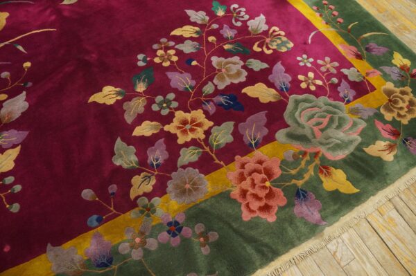 Plush magenta rug with multicolored floral design and wide moss green border rests on wood flooring.
