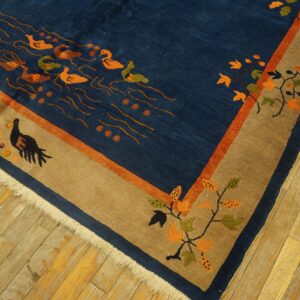 A dark blue rug with orange swimming birds and a tan border sits on worn hardwood floors.