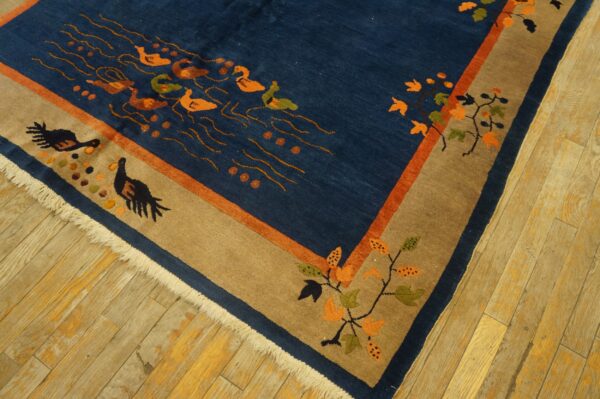 A dark blue rug with orange swimming birds and a tan border sits on worn hardwood floors.