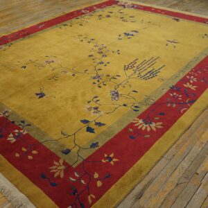 Gold rug with wide red and olive borders displays scattered floral and vine patterns on distressed wood flooring.