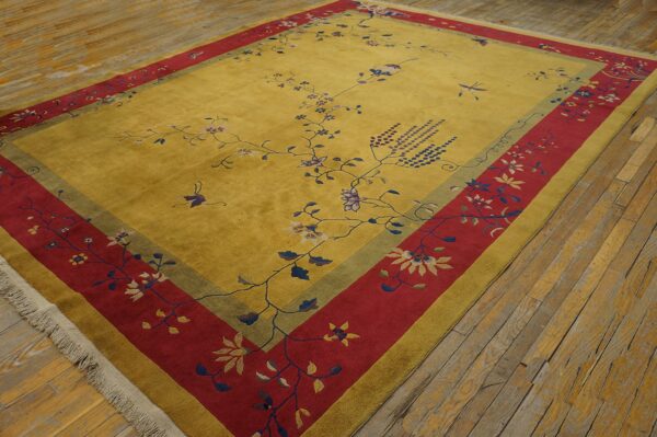 Gold rug with wide red and olive borders displays scattered floral and vine patterns on distressed wood flooring.