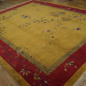 Yellow rug with dense red and green borders, patterned with delicate floral vines, sitting on wood plank flooring.
