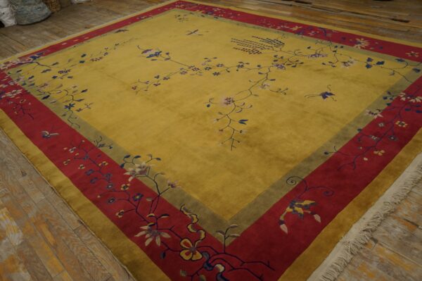 Yellow rug with dense red and green borders, patterned with delicate floral vines, sitting on wood plank flooring.