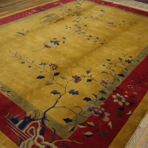 Gold rug with a stylized floral vine pattern and wide red and olive borders on distressed wooden floors.