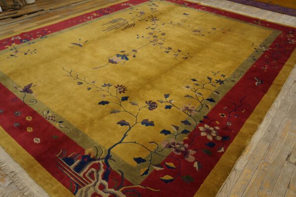 Gold rug with a stylized floral vine pattern and wide red and olive borders on distressed wooden floors.