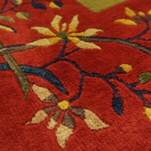 Textured close-up of a plush red rug featuring gold floral designs and deep blue vines.