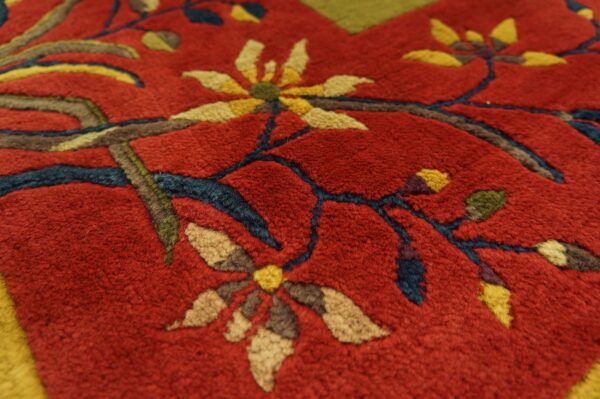 Textured close-up of a plush red rug featuring gold floral designs and deep blue vines.