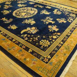 Plush navy and gold rug featuring ornate floral patterns and a geometric key border on hardwood flooring.