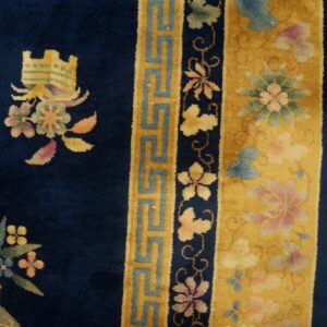 Navy rug with colorful floral motifs and yellow geometric borders seen next to rustic wood planks.