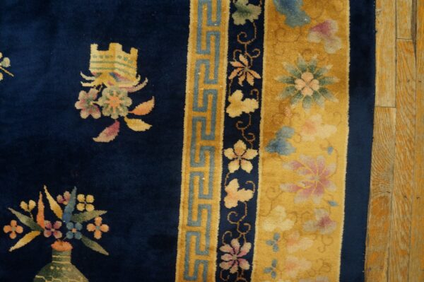 Navy rug with colorful floral motifs and yellow geometric borders seen next to rustic wood planks.
