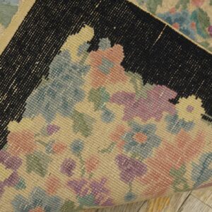 Pastel floral rug folded back, showing the flat-woven reverse side, black border, and light wood floor.