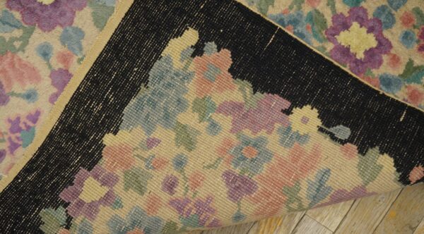 Pastel floral rug folded back, showing the flat-woven reverse side, black border, and light wood floor.