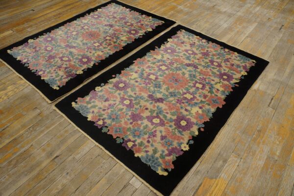 Two matching rugs with colorful floral patterns and black borders displayed on distressed light wooden flooring.