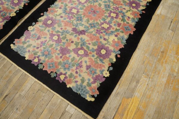 Pastel floral rug with dusty pink, purple, and blue blossoms bordered in black on worn wooden flooring.