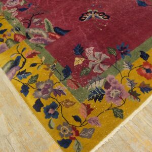 Colorful floral rug corner showing a red field, yellow border, and complex botanical motifs on light wood floors.