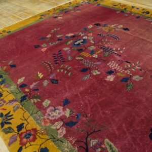 Distressed magenta rug with a yellow border features intricate multicolor floral and bird patterns on wood flooring.
