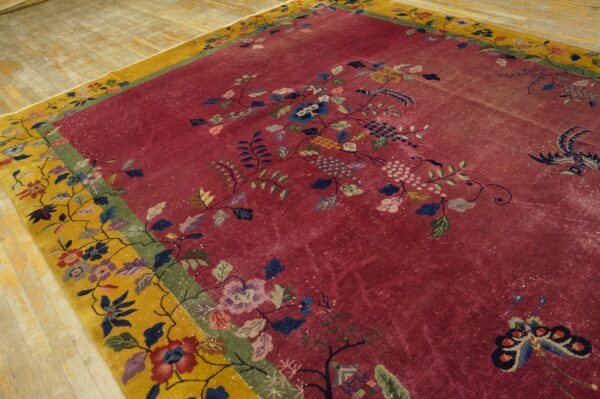 Distressed magenta rug with a yellow border features intricate multicolor floral and bird patterns on wood flooring.