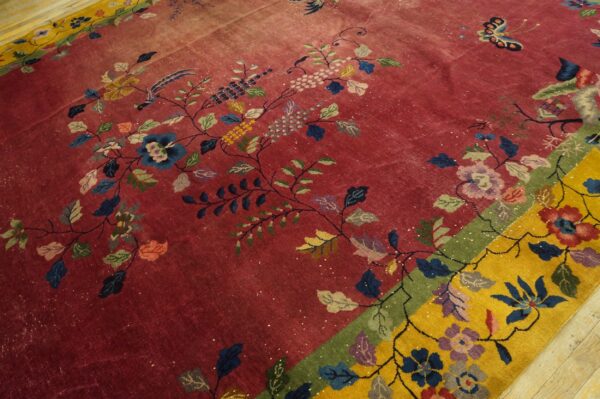 Low-pile red rug featuring colorful floral vines, birds, and a butterfly, bordered by bright yellow on wood floor.