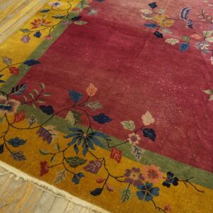 Colorful floral rug with a magenta field and yellow border sits on aged wood plank flooring.